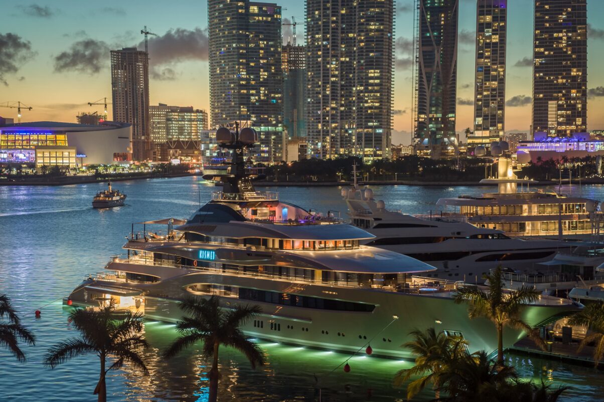 A full marina with superyachts, lit up by numerous different coloured lights.
